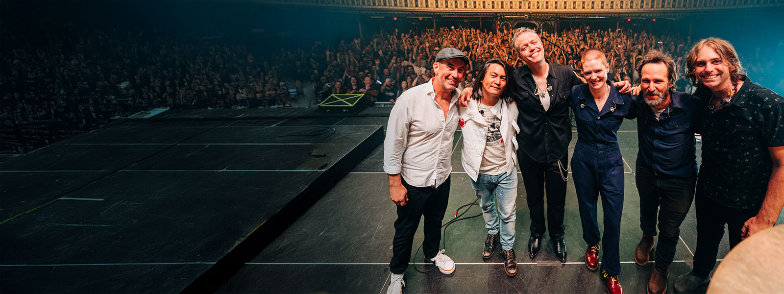 Jason Isbell and the 400 Unit standing with arms around each other with a sold out venue behind them