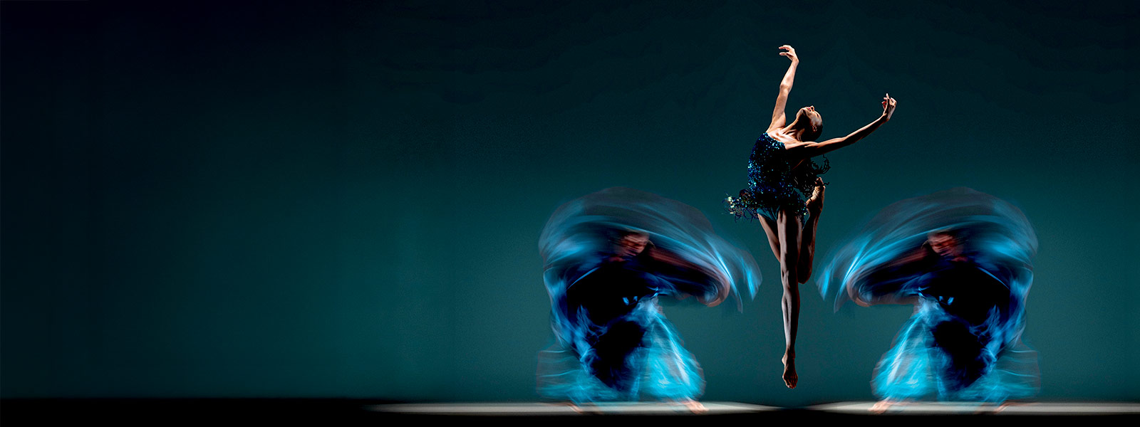 Alonzo King LINES Ballet dancer jumping upward with arms extended above, with blurred dancers in motion on either side