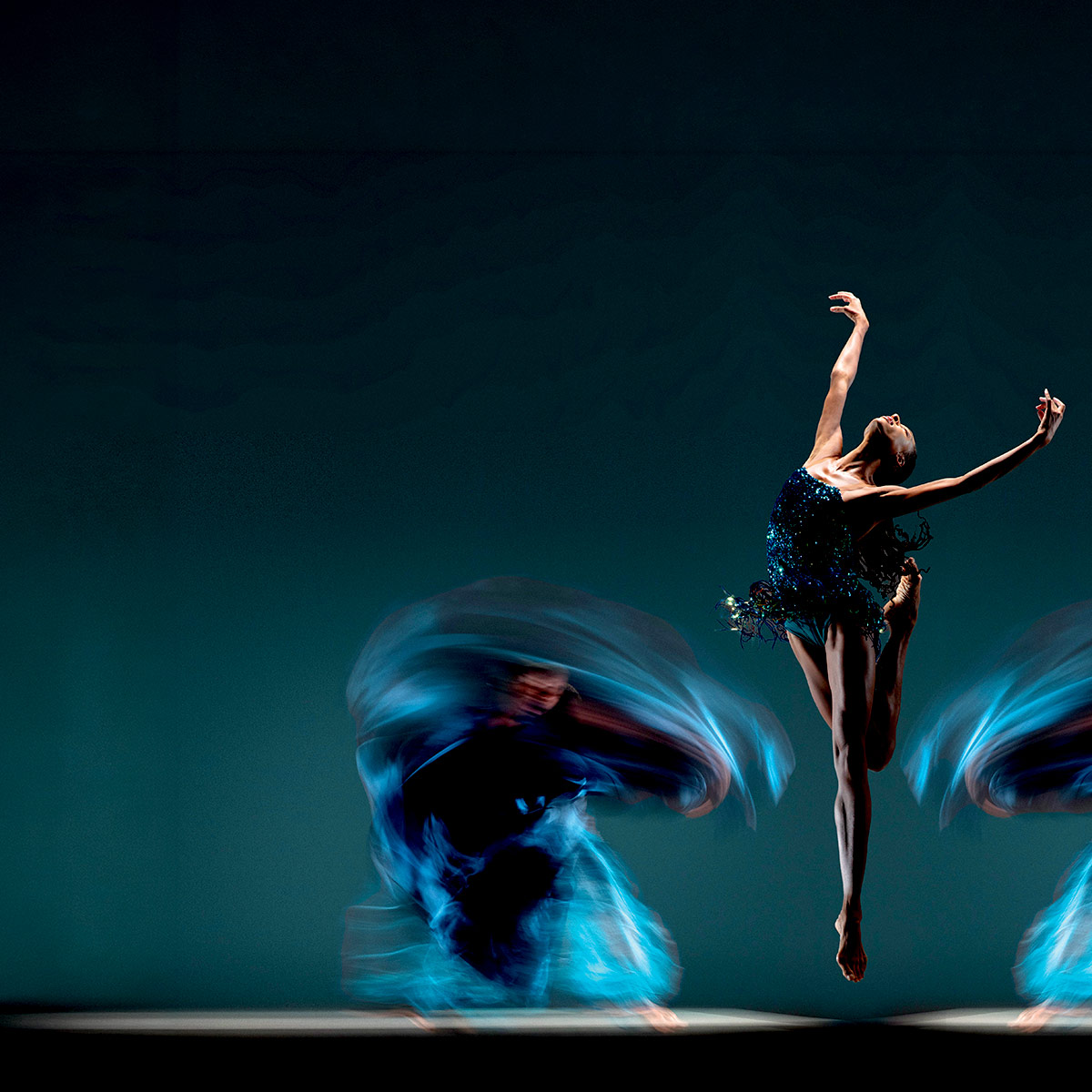 Alonzo King LINES Ballet dancer jumping upward with arms extended above, with blurred dancers in motion on either side