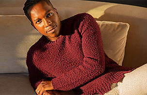 Leslie Odom Jr. wearing a burgundy top, sitting on a cream-colored couch