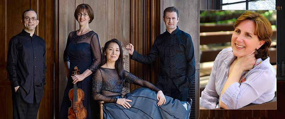 All four member of the quartet, posing in matching black outfits, one of which is holding a violin
