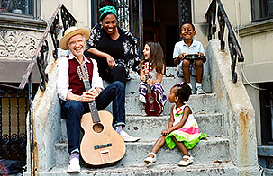 Dan + Claudia Zanes sit on the stoop of a brownstone home, sharing a laugh with three children