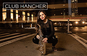 Alexa Tarantino, dressed in a black and holding her saxophone, crouches on the pavement of a city intersection at nighttime