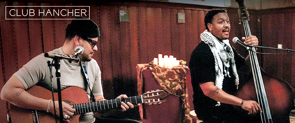 Brian Quijada + Nygel D Robinson playing guitar and cello in front of microphone with Club Hancher text treatment in upper left corner