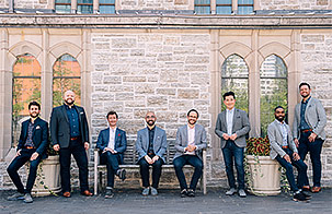 The Cantus boys pose against a light-colored brick wall in jeans and sport coats