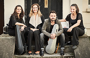 Elias String Quartet sitting outside on a stoop with their instruments in cases looking at the camera smiling