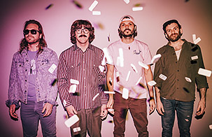 Goose band members standing against a pink gradient background. Confetti is floating down around them