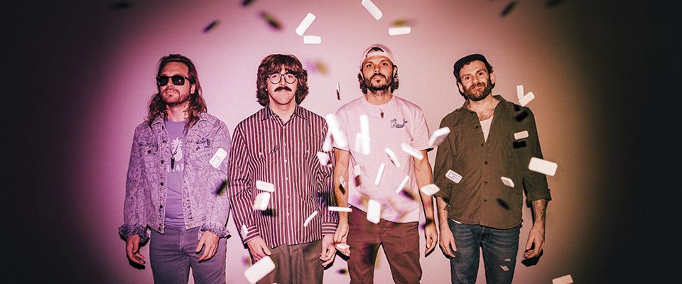 Goose Goose band members standing against a pink gradient background. Confetti is floating down around them