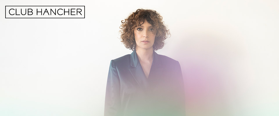 Gaby Moreno standing facing the camera in a blue suit. Club Hancher text treatment in upper left corner