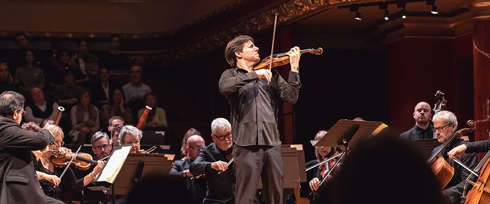 Joshua Bell and Academy of St. Martin in the Fields Joshua Bell playing while standing in the middle of an ensemble sitting down and playing string instruments