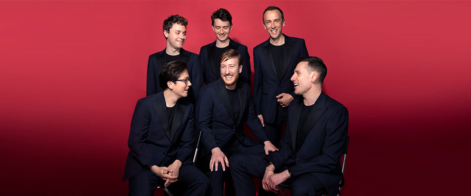 The King's Singers looking at each other laughing against a red background. All members are wearing a black suit
