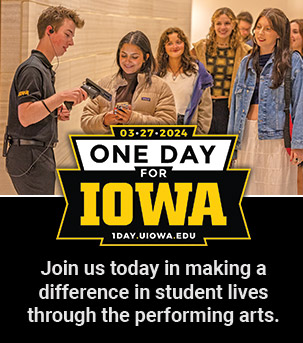 Student usher scanning tickets for a performance with a line of young UI students waiting for admission. One day for Iowa logo 