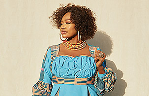 Oumou Sangaré center focus looking to the left against a tan background wearing light blue, yellow, and red colors. 