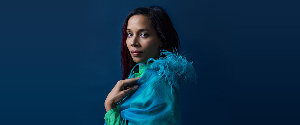 Side profile of Rhiannon Giddens waist up in a blue outfit against a blue background
