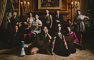 Roomful of Teeth ensemble sitting in a extravagant foyer looking at the camera.