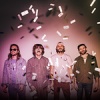 Goose band members standing against a pink gradient background. Confetti is floating down around them