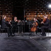 JACK Quartet sitting in half circle in all black clothing playing their instruments on stage