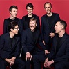 The King's Singers looking at each other laughing against a red background. All members are wearing a black suit