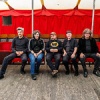 Magnetic Fields band members sitting in a line in red auditorium seats. All members are wearing black shirts and looking at the camera