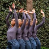 Trisha Brown dancers next to greenery with their hands above their head