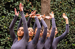 Trisha Brown dancers next to greenery with their hands above their head