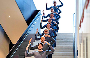Trisha Brown dancers standing in a line up stairs with their hands raised above their head
