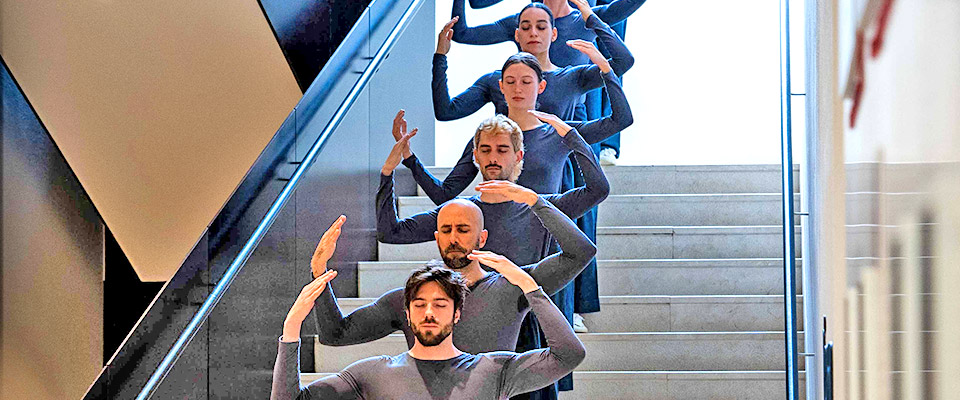 Trisha Brown Dance Company dancers standing in a row with hands above their head
