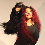 Chaka Khan in a black dress against a beige background. 