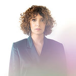 Gaby Moreno standing facing the camera in a blue suit. Club Hancher text treatment in upper left corner