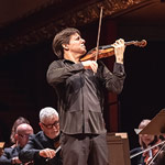 Joshua Bell playing while standing in the middle of an ensemble sitting down and playing string instruments