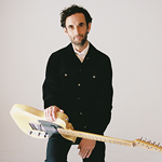 Julian Lage holding guitar against blue gradient 