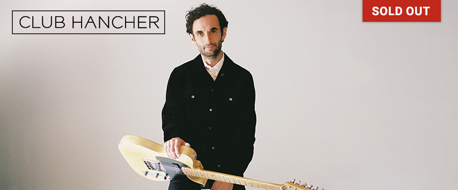 Julian Lage holding guitar against blue gradient 